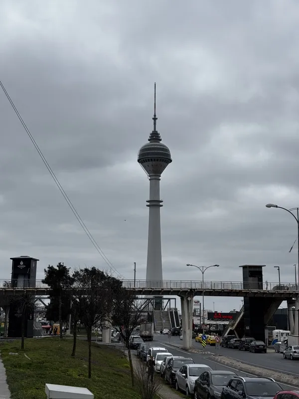 A slender TV tower rising above a footbridge under an overcast sky